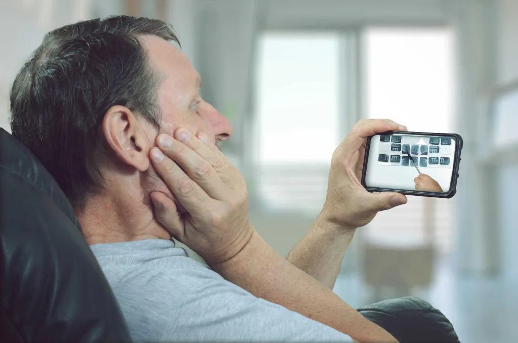 man holding mouth viewing smart phone of dental x rays virtual dentist visit